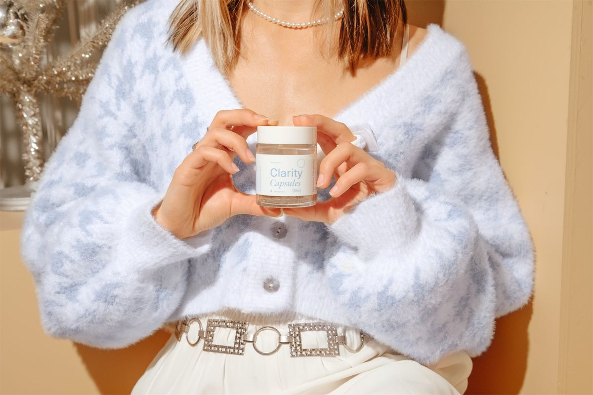 Model in a fluffy blue cardigan holding a Clarity Capsules jar at her waist