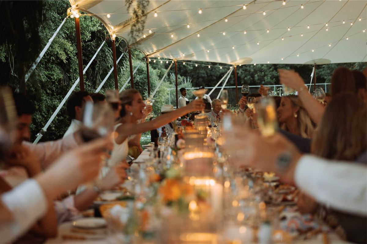 Guests raising a toast along the candlelit table beneath a string-lit tent