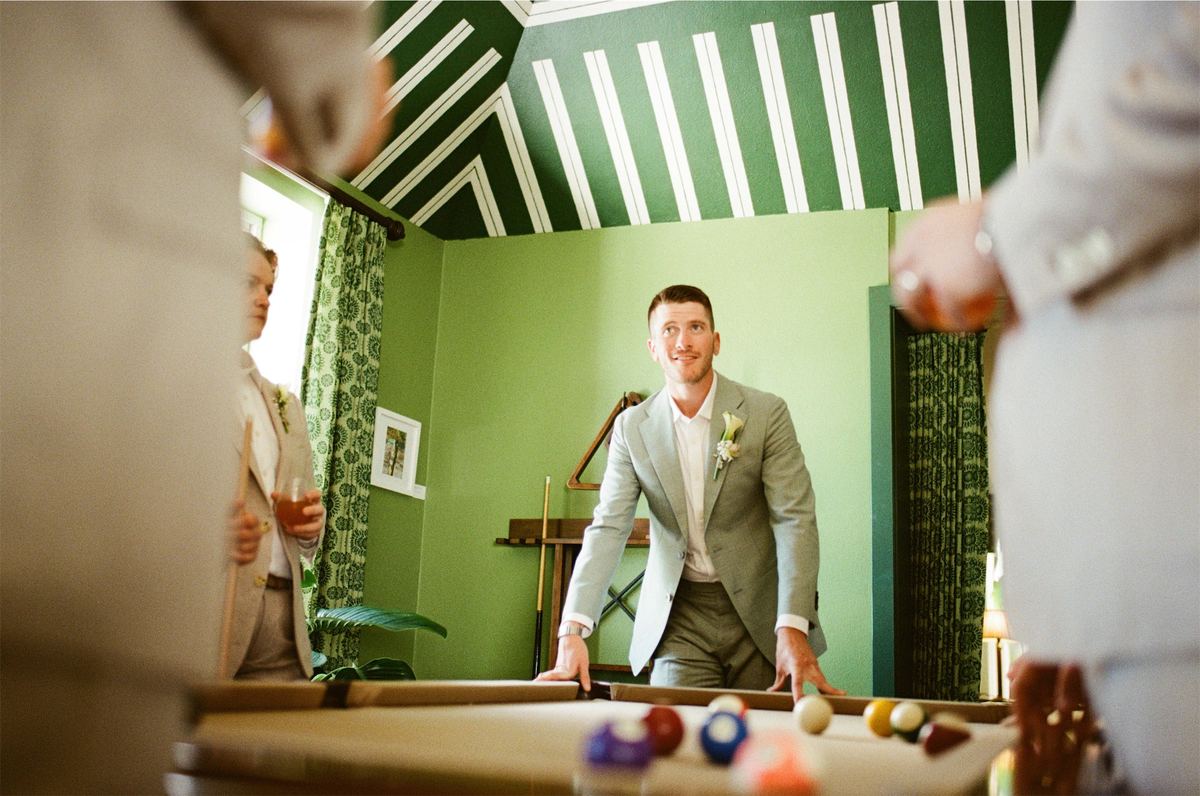 Groom in a sage green suit standing at the pool table in a green games room
