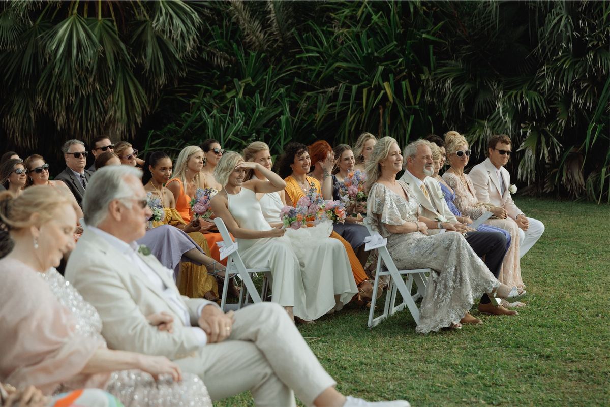 Guests seated on white chairs watching the ceremony in a tropical garden