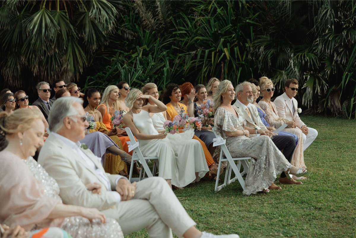 Guests seated on white chairs watching the ceremony in a tropical garden
