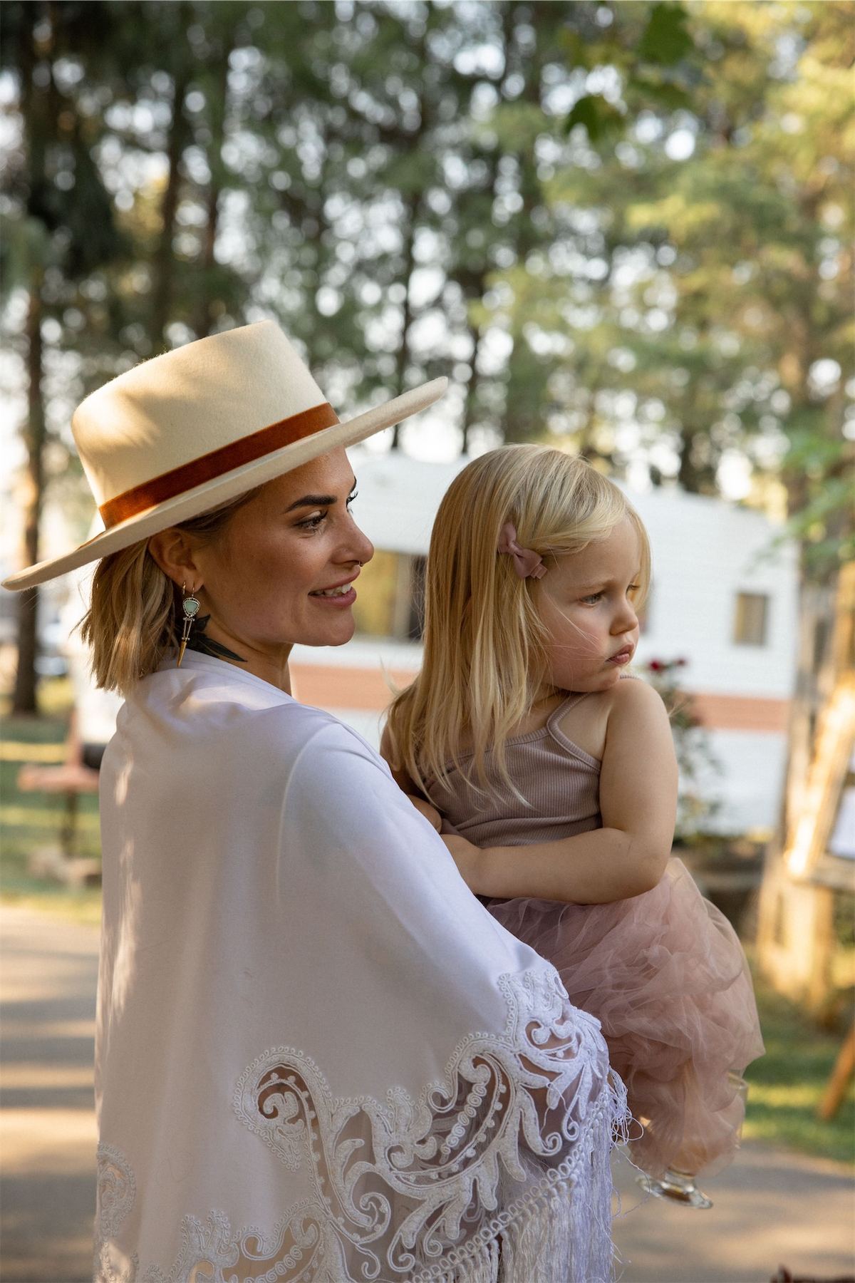 Bride in a hat holding a small child on her hip at the outdoor reception