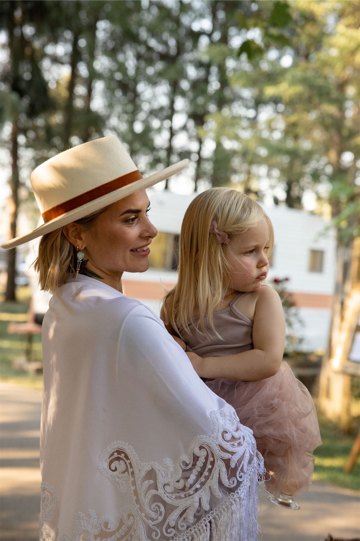 Bride in a hat holding a small child on her hip at the outdoor reception