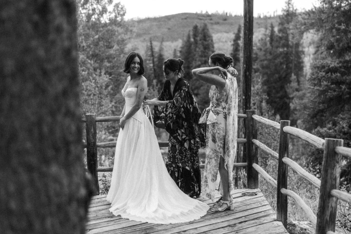 Devin's mother and a friend fix her gown on the wooden deck above the valley at a mountain ranch among the aspens, black and white