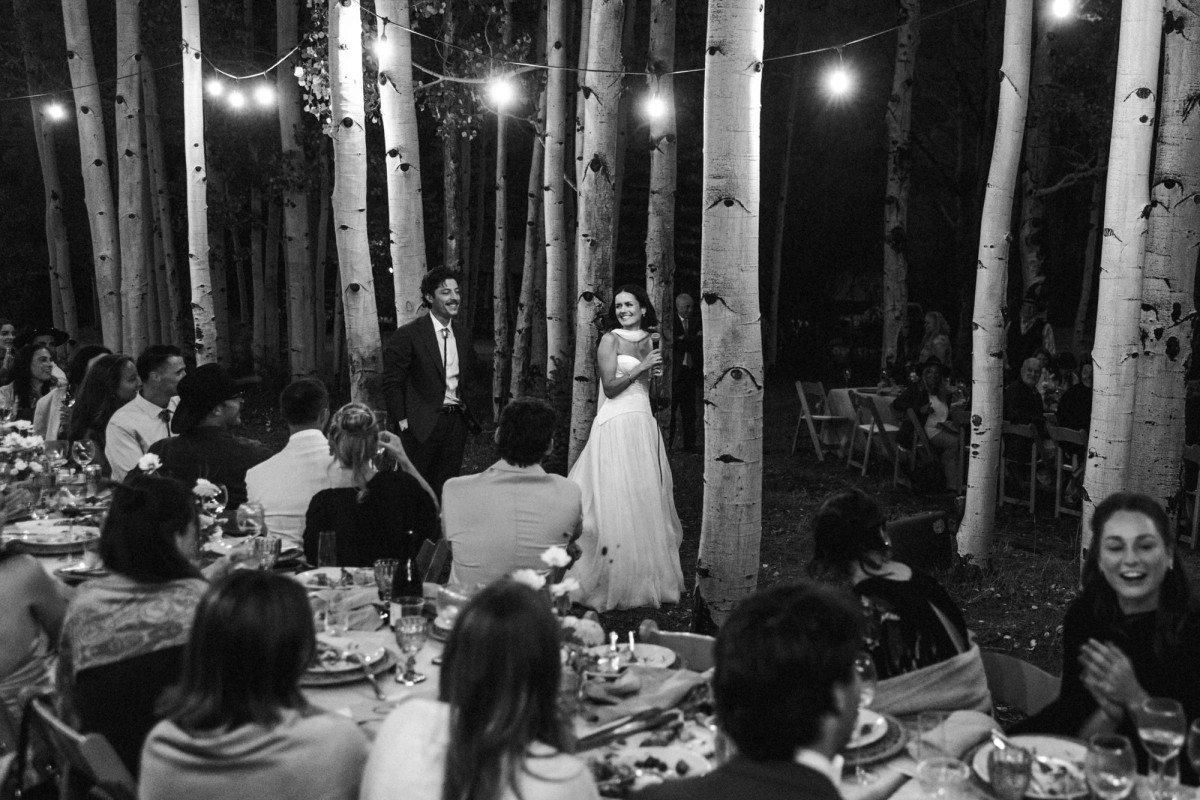 Devin and Owen stand among the tables under the lights in the aspens at a mountain ranch among the aspens