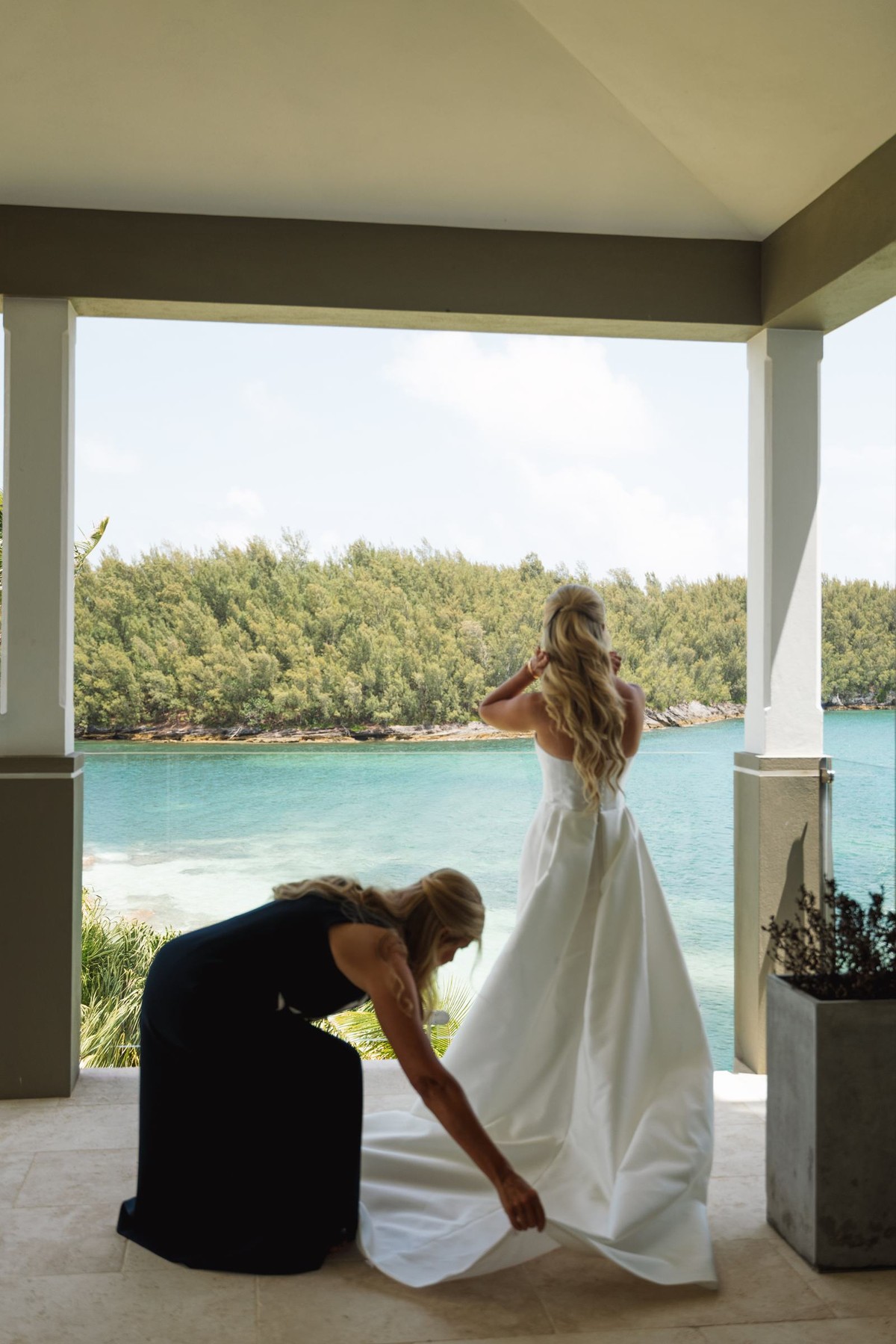 A bridesmaid adjusts Paige's train on the porch looking out to the water on Hawkins Island, Bermuda