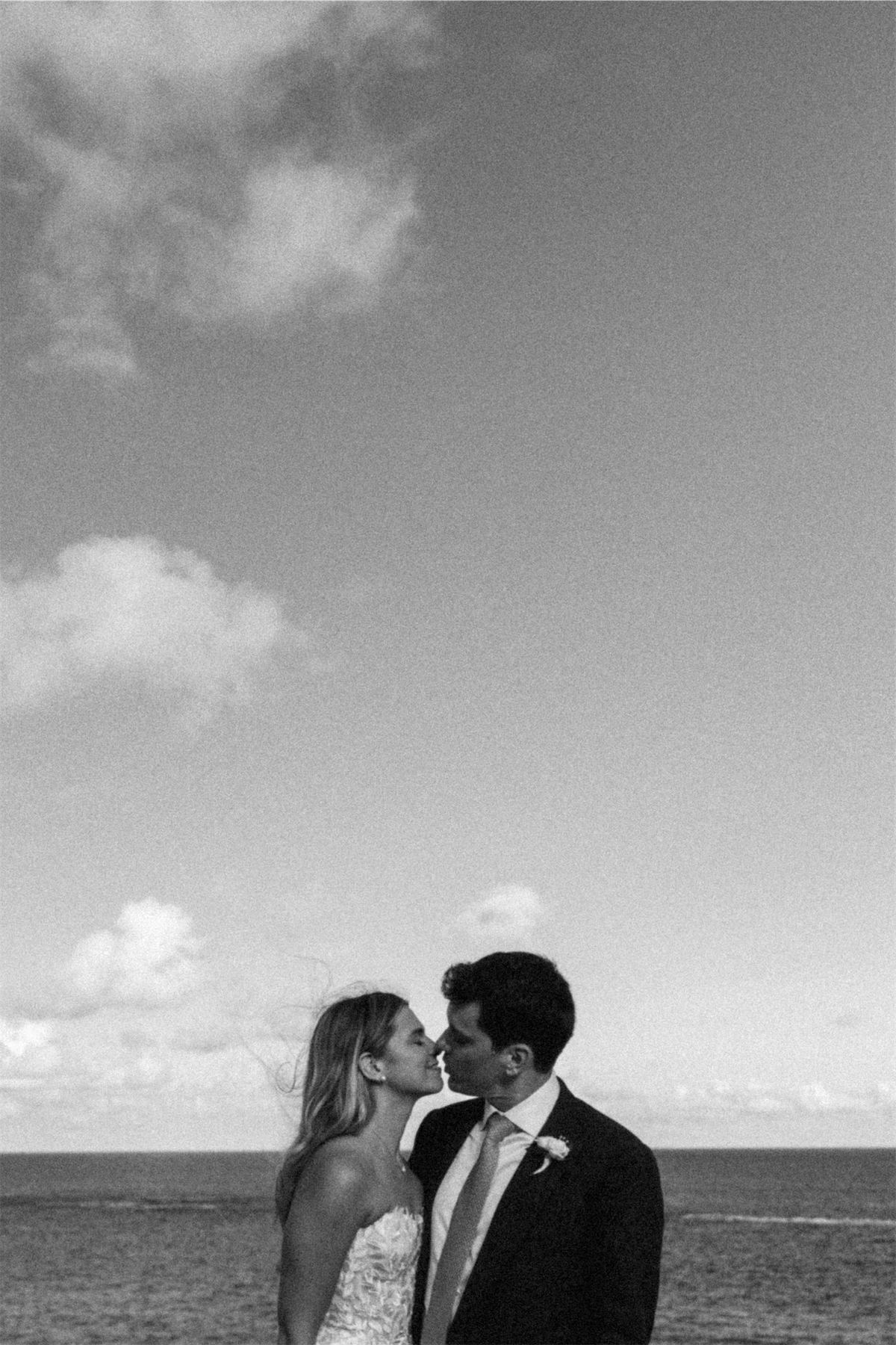 Black and white of the bride and groom leaning in to kiss with the open ocean behind them