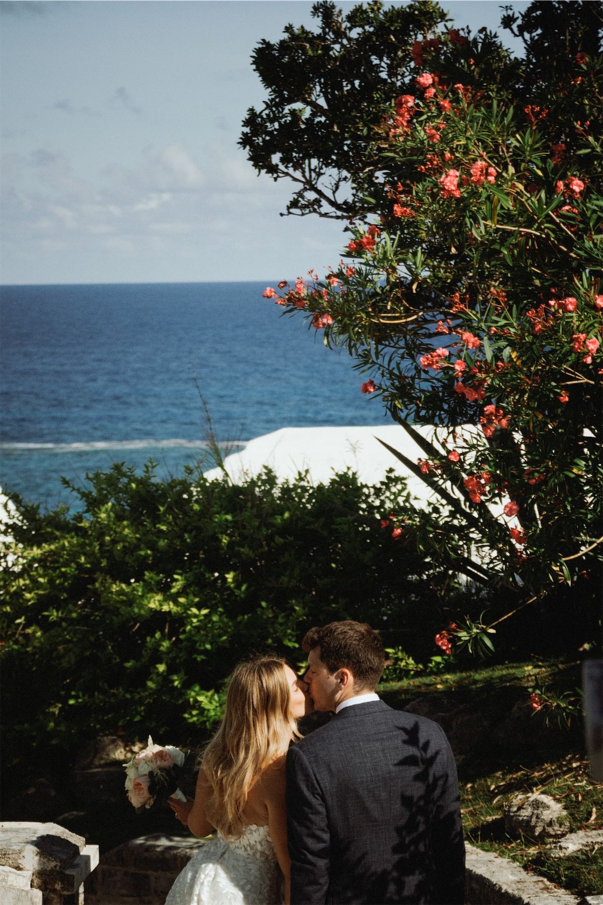 Bride and groom looking out to the ocean past a flowering oleander