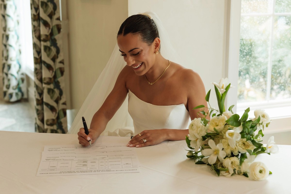 Bride laughing as she signs the marriage register beside her bouquet at Rosewood Bermuda