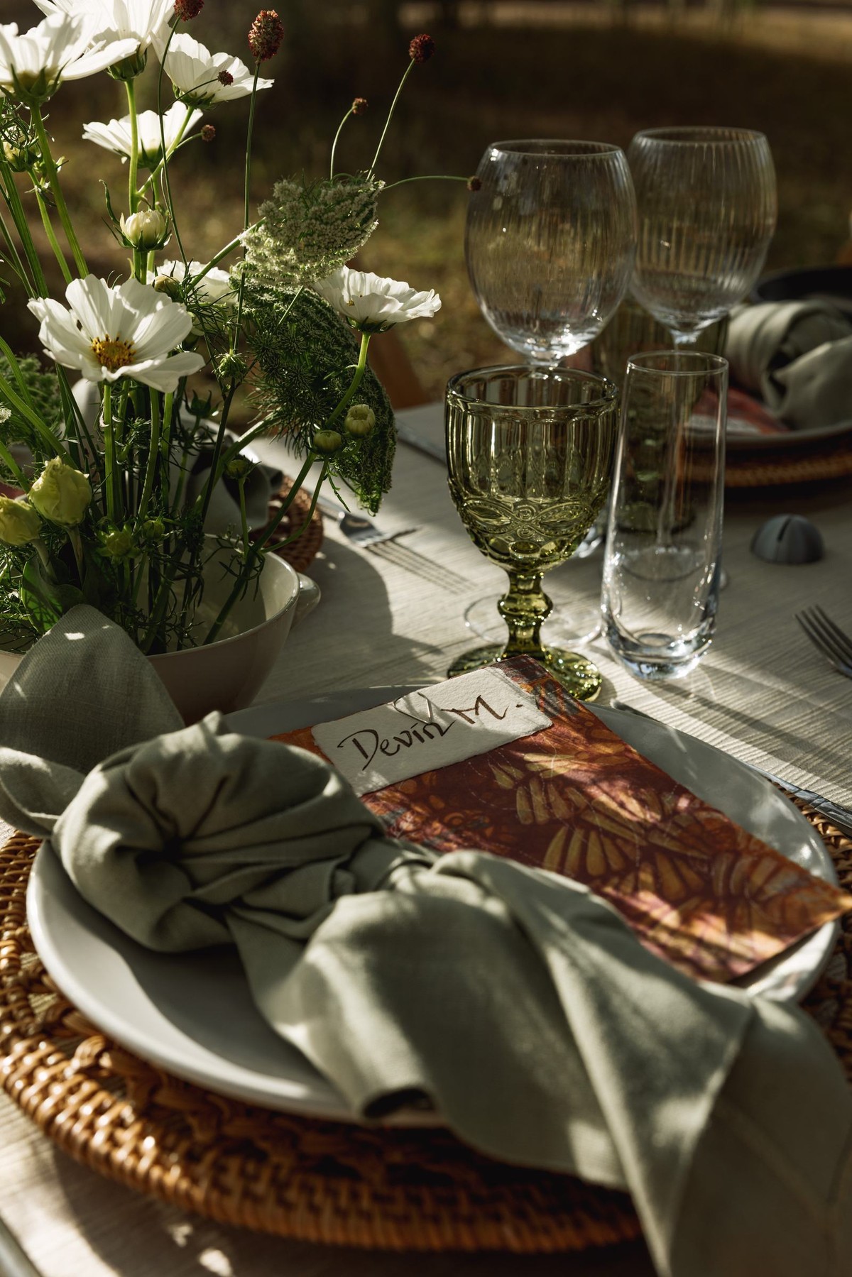 Hand lettered place card on a woven charger with a sage napkin at a mountain ranch among the aspens