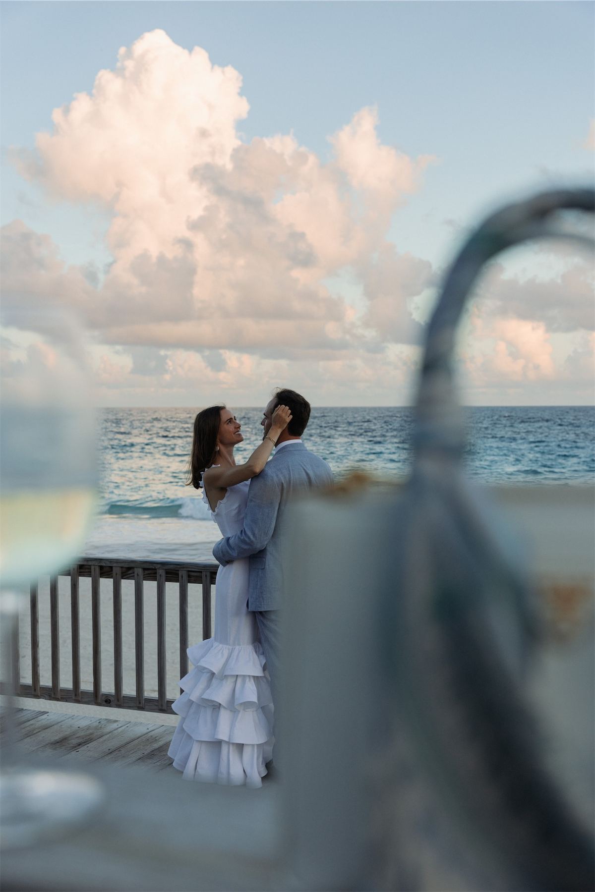 Guest in a blue tiered dress seen past a round mirror on a balcony over the sea