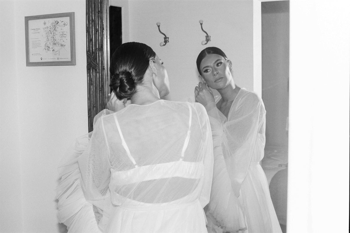 Black and white frame of the bride and a bridesmaid getting ready together in sheer white robes