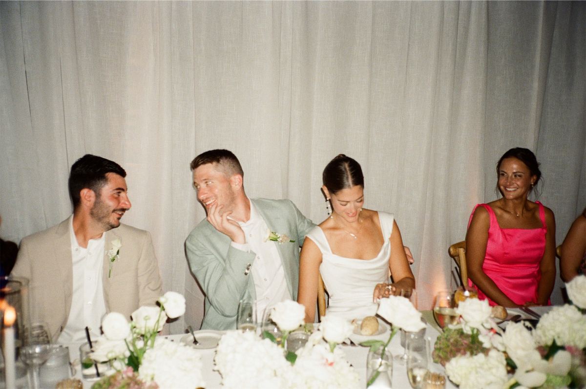 Bride and groom laughing with guests at the candlelit reception table