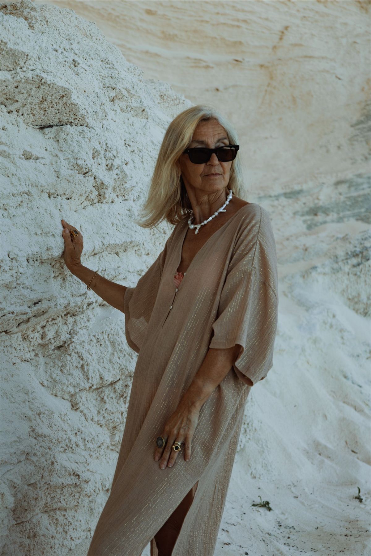 Model in sunglasses and a sand kaftan resting a hand on the white cliff face