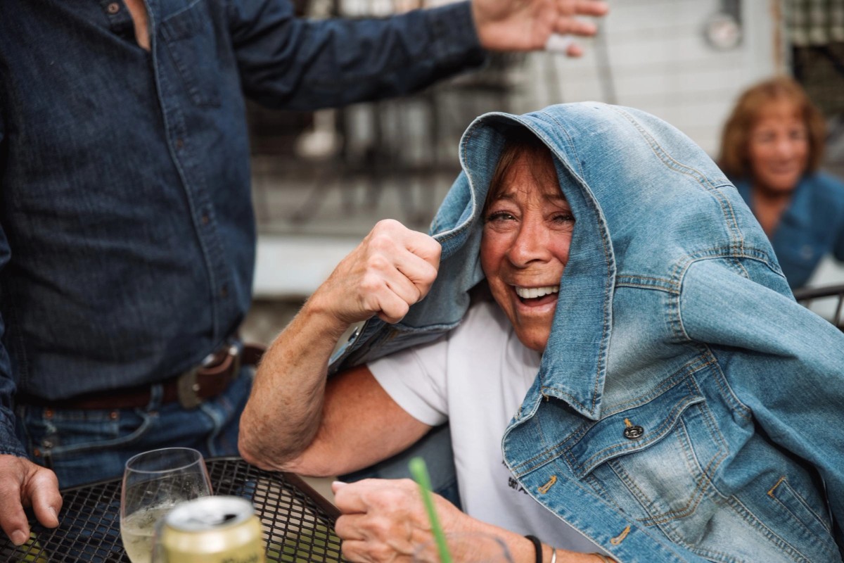 A guest laughs with a denim jacket pulled over her head at the welcome dinner at a mountain ranch among the aspens