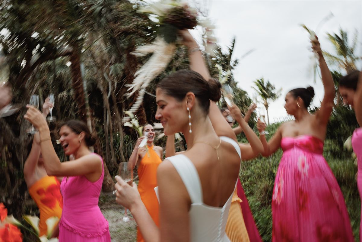 Bridesmaids in bright pink and orange raising their glasses around the bride