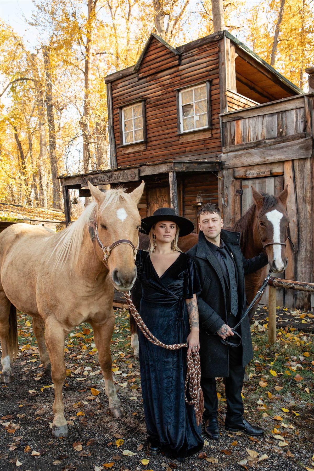 Bride and groom standing with a palomino horse outside a weathered barn