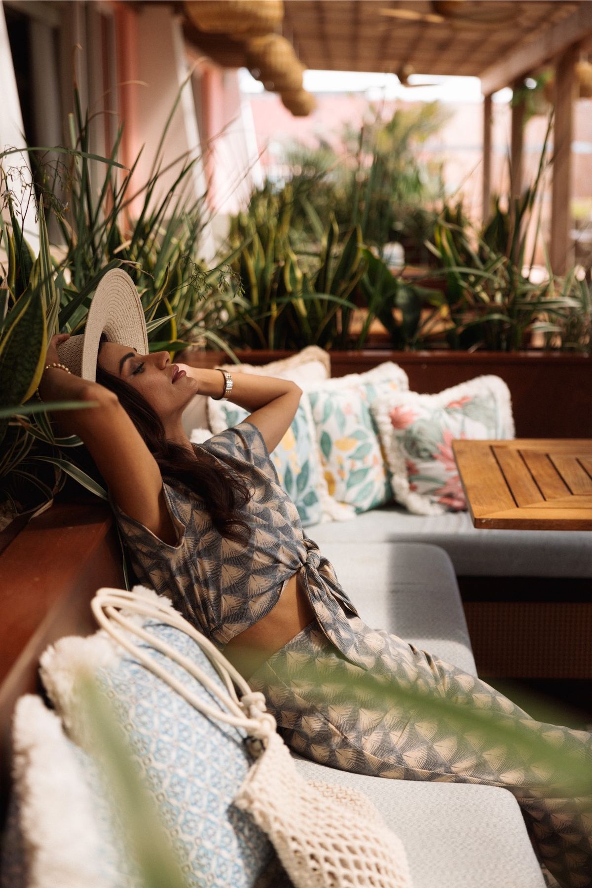 Model stretched out on an outdoor daybed in a printed cover-up among potted plants