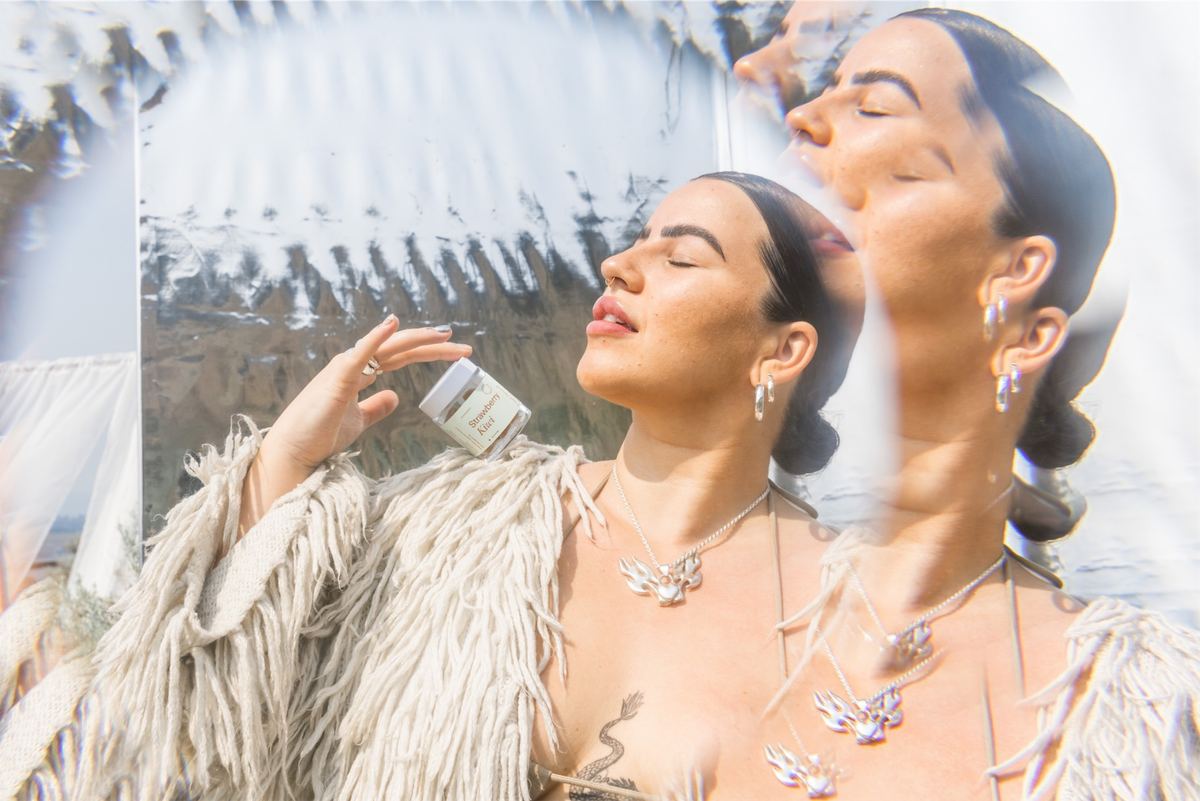 Model with eyes closed holding a capsule jar, her face repeated in angled mirrors