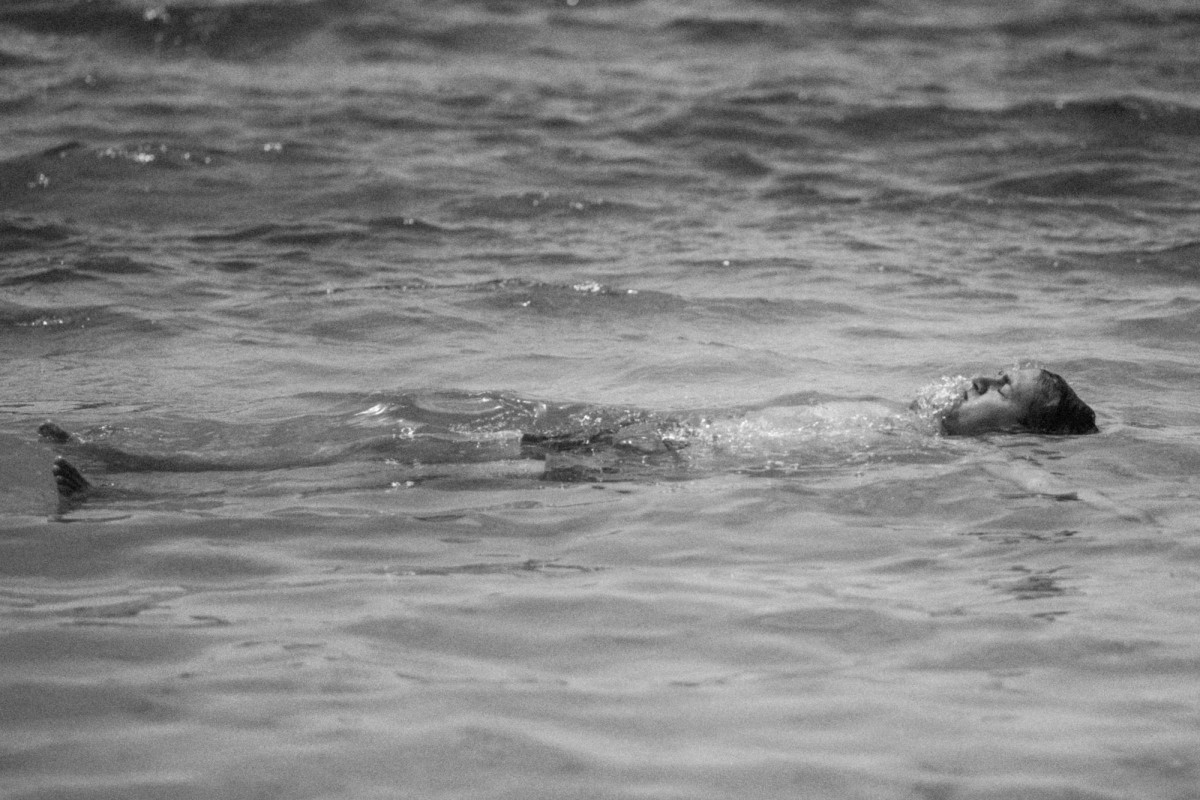 A groomsman floats on his back in the open water on Hawkins Island, Bermuda, black and white