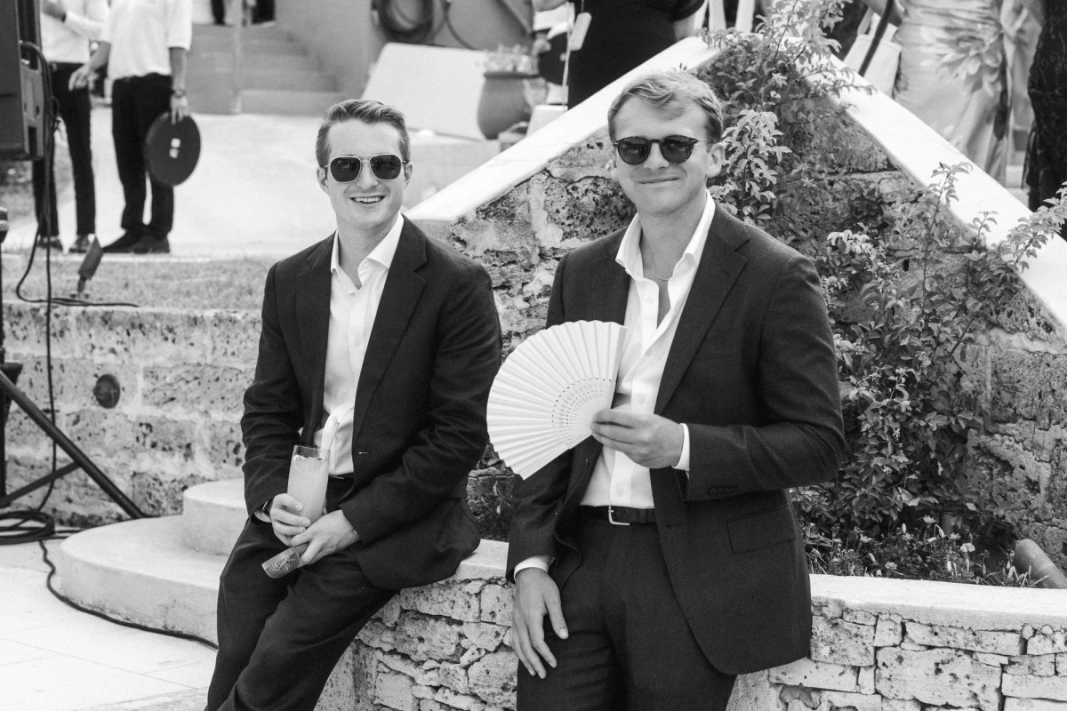 Two guests in sunglasses wait for the ceremony with a paper fan on Hawkins Island, Bermuda, black and white