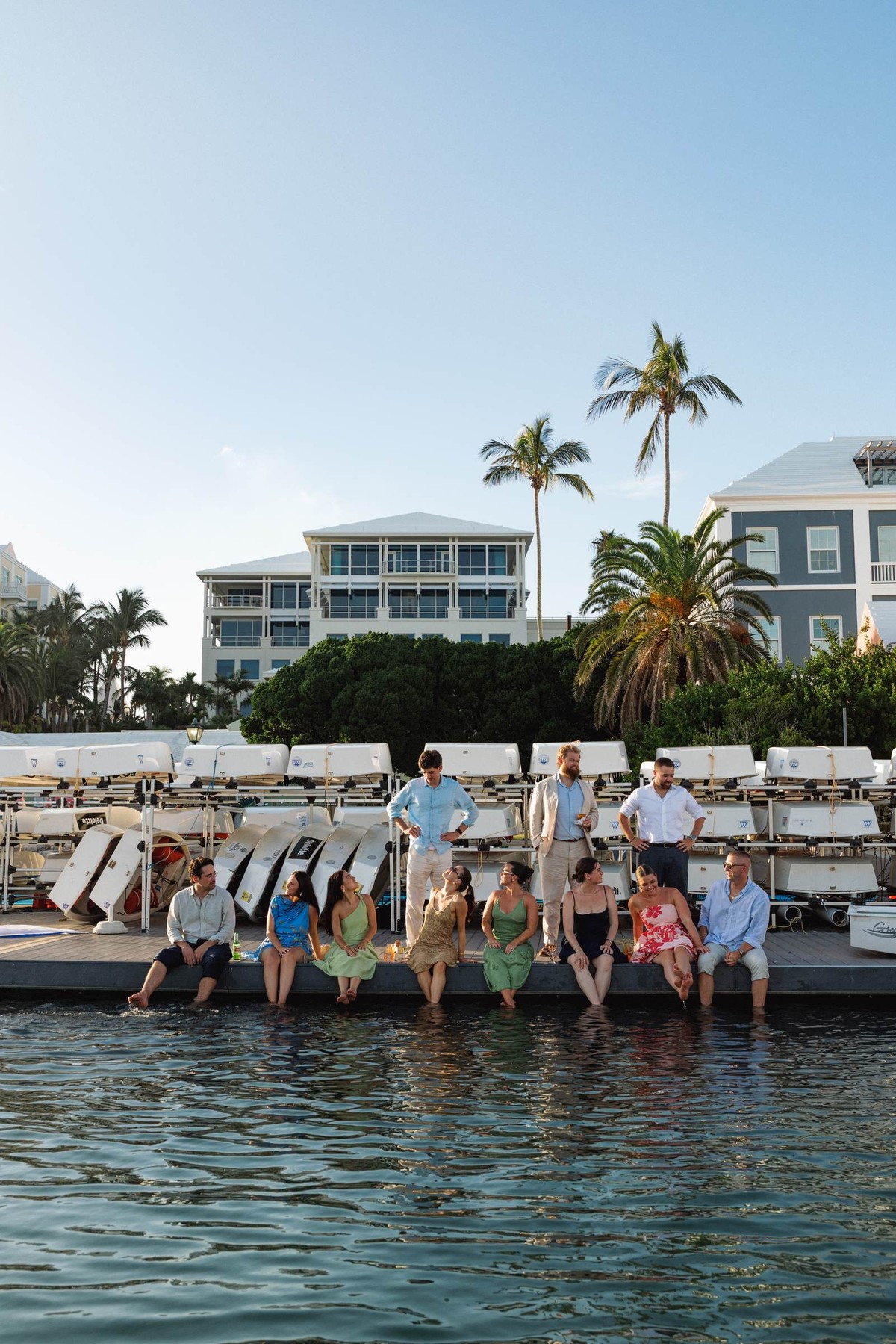 The wedding party lines the dock edge with feet in the water at the welcome party in Bermuda