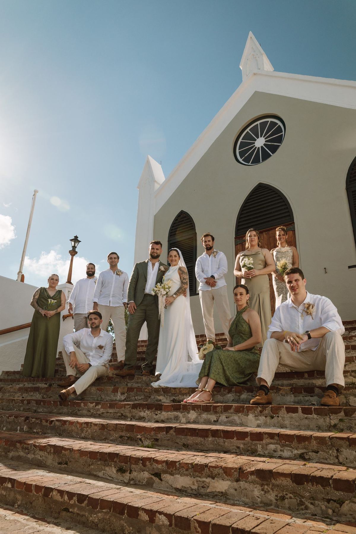 Wedding party seated together on the steps of a white Bermuda church