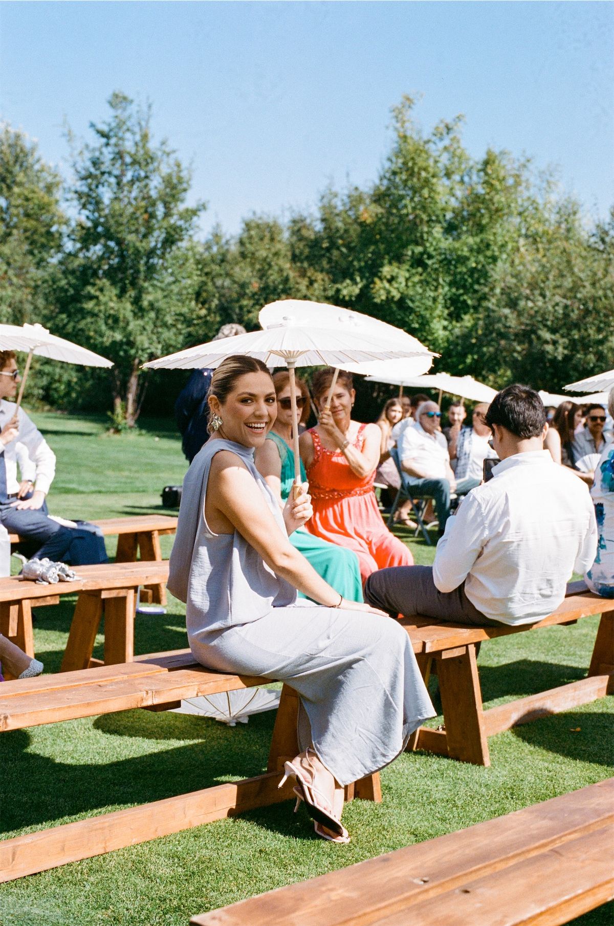 Guests seated at picnic tables under white umbrellas during outdoor cocktail hour