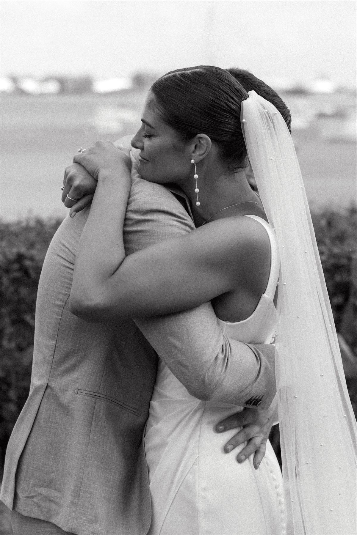 Black and white of the bride in her veil holding a guest in a long hug