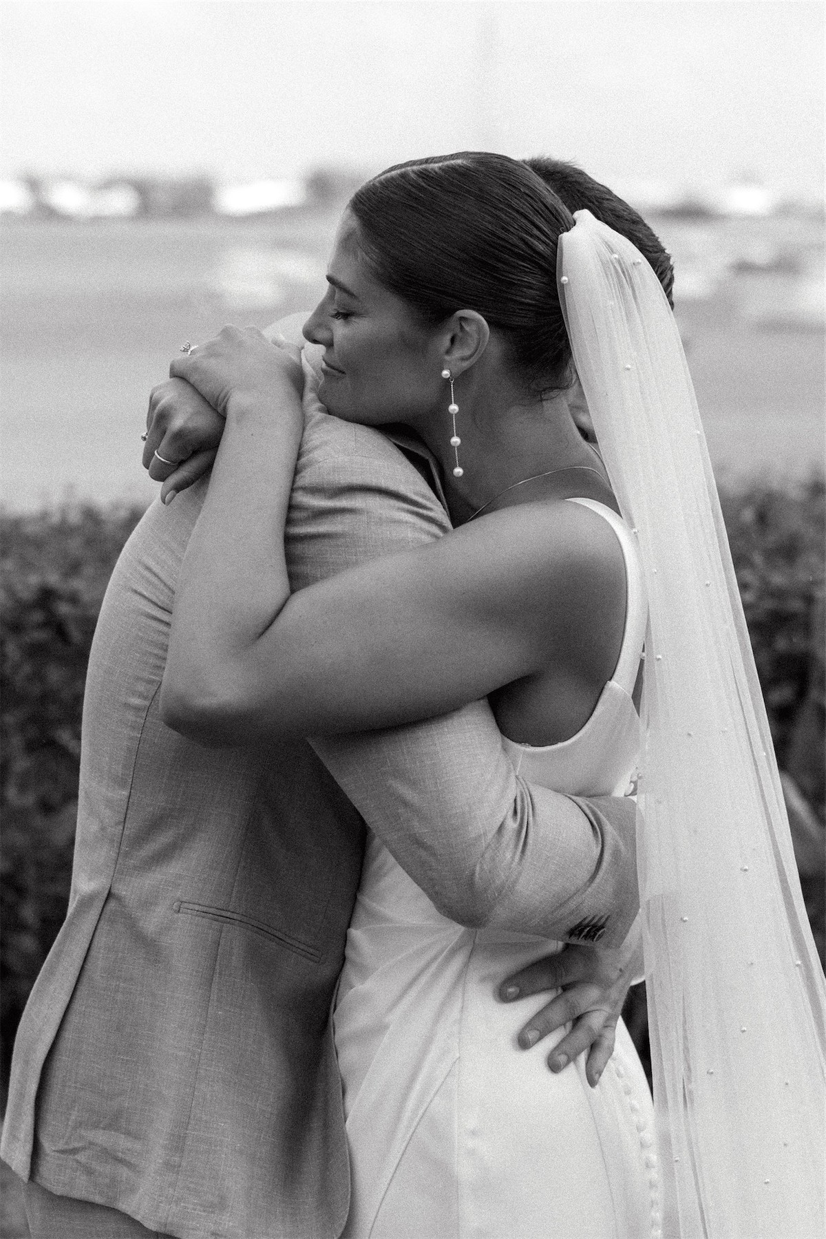 Black and white of the bride in her veil holding a guest in a long hug