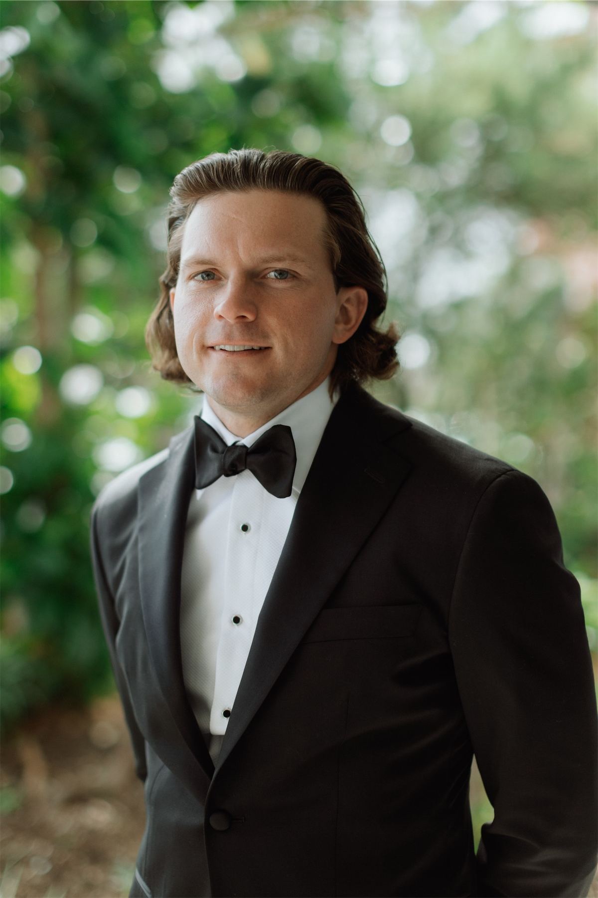 Portrait of the groom in black tuxedo and bow tie framed by garden greenery