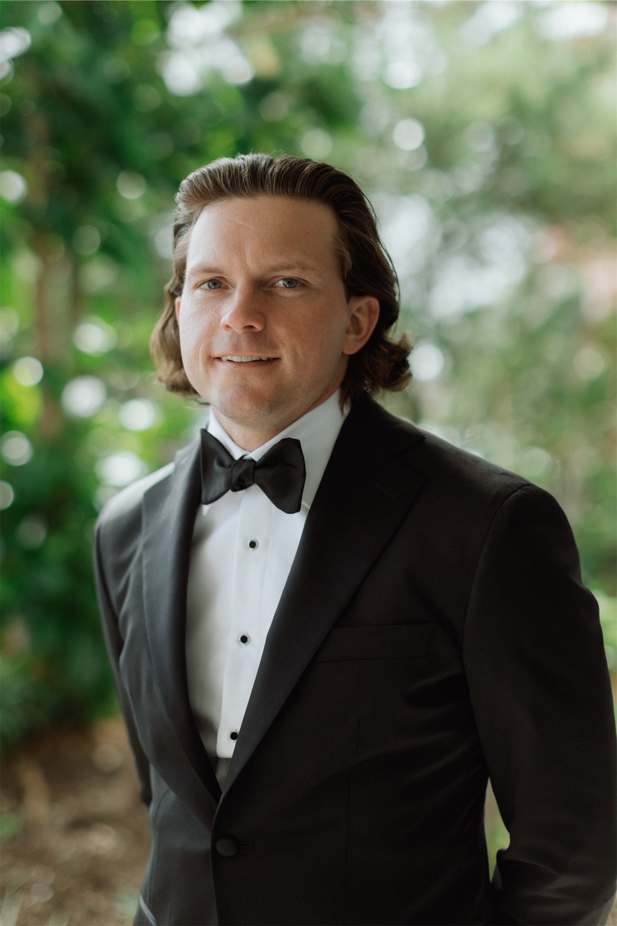 Portrait of the groom in black tuxedo and bow tie framed by garden greenery