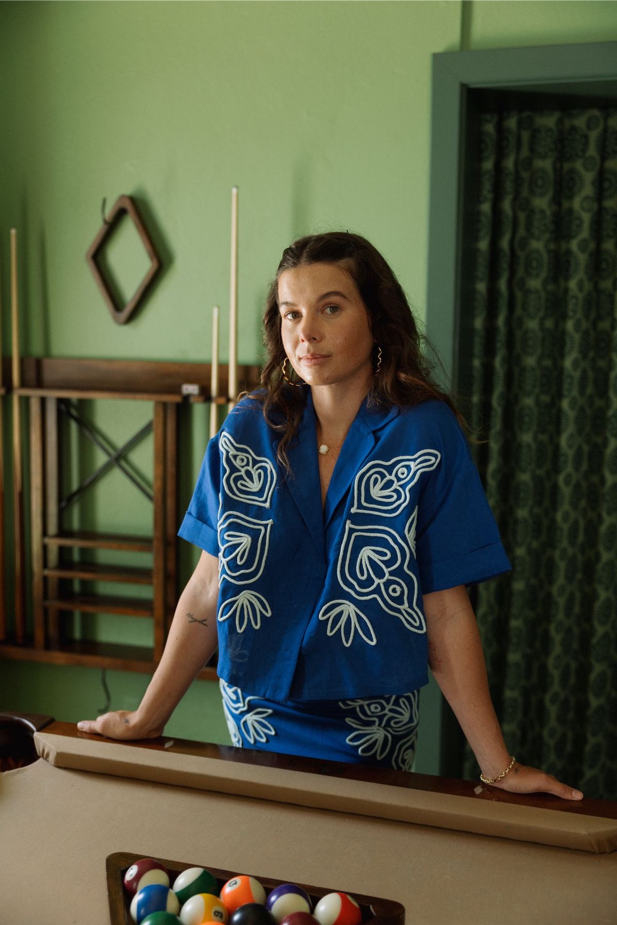 Model in an embroidered blue camp shirt leaning on a pool table in a green room