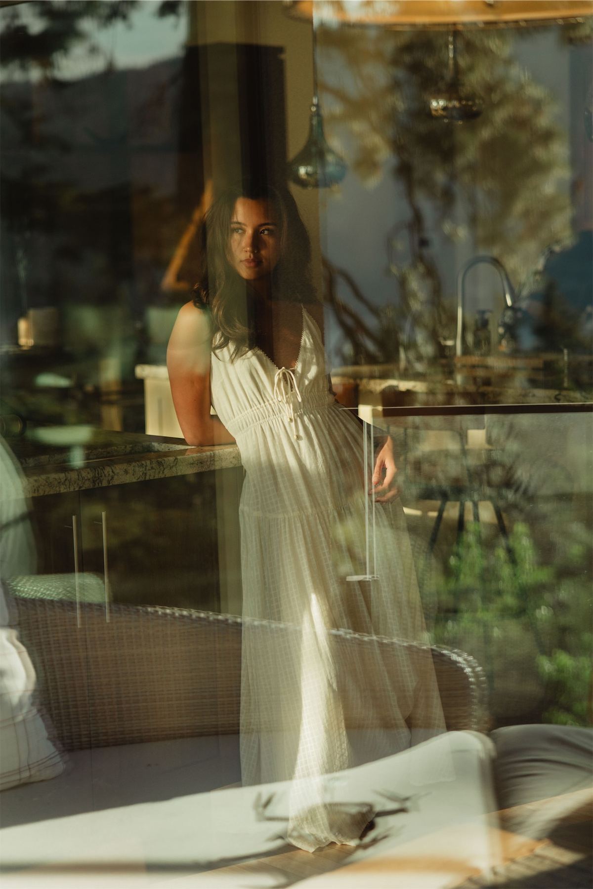 Woman in a long white dress reflected in the glass wall of a modern lodge