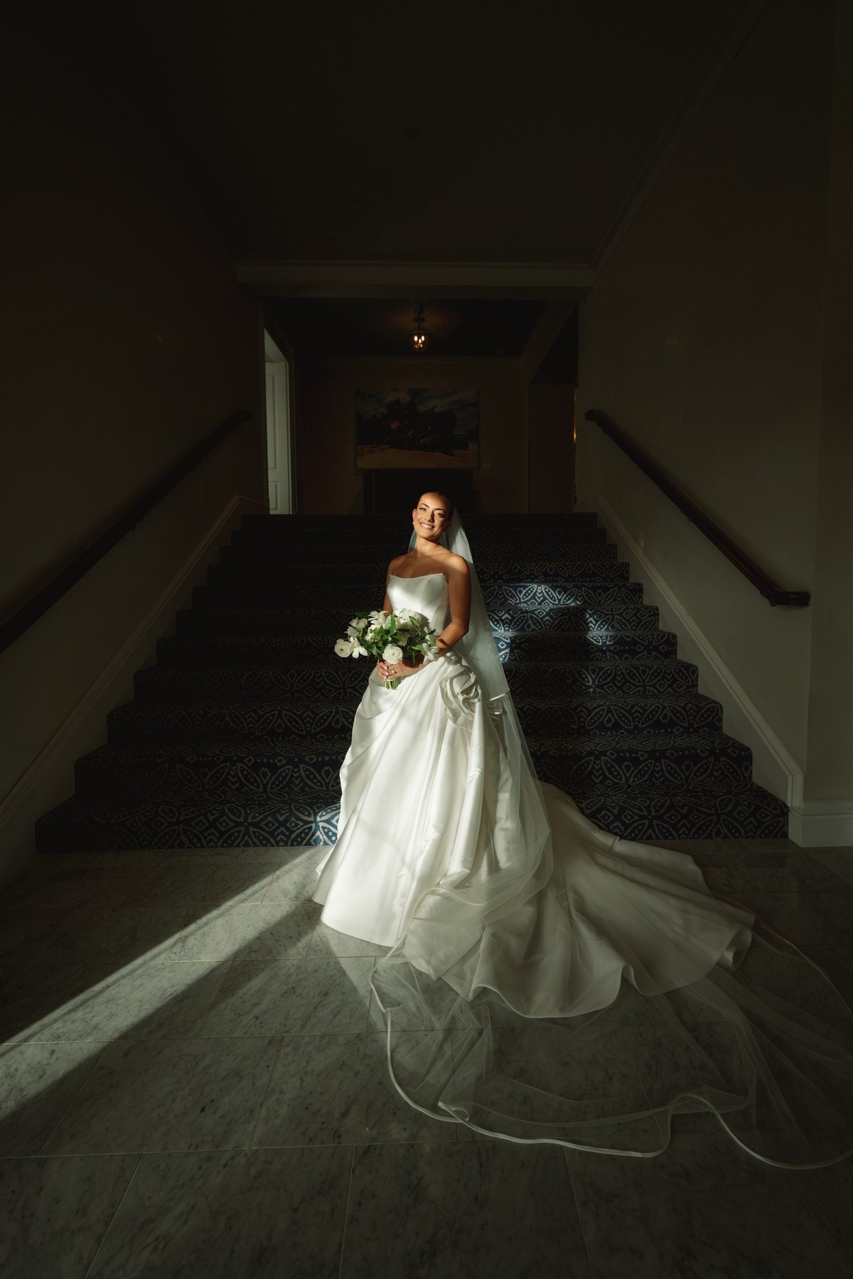 Bride on a dark staircase with her veil pooled in a pocket of light at Rosewood Bermuda