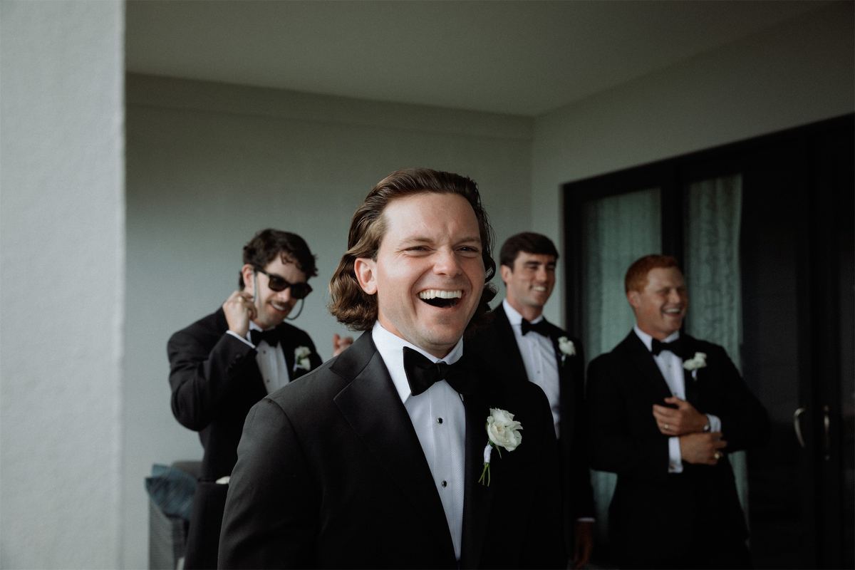 Groom laughing with his groomsmen while they get ready in a sunlit room