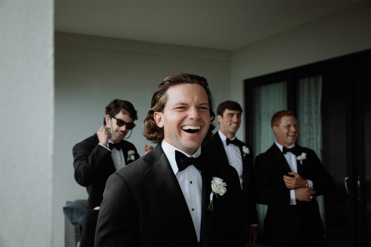 Groom laughing with his groomsmen while they get ready in a sunlit room