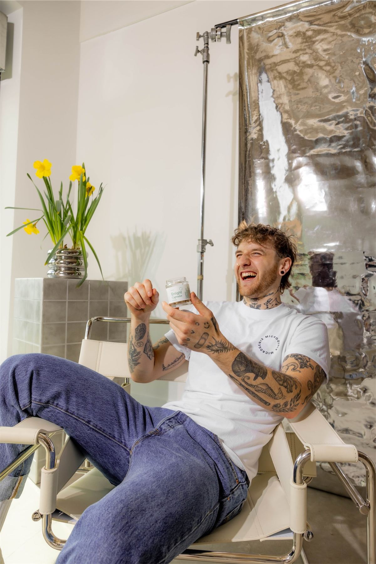Man in a white tee lying back in a bathtub holding a jar of capsules