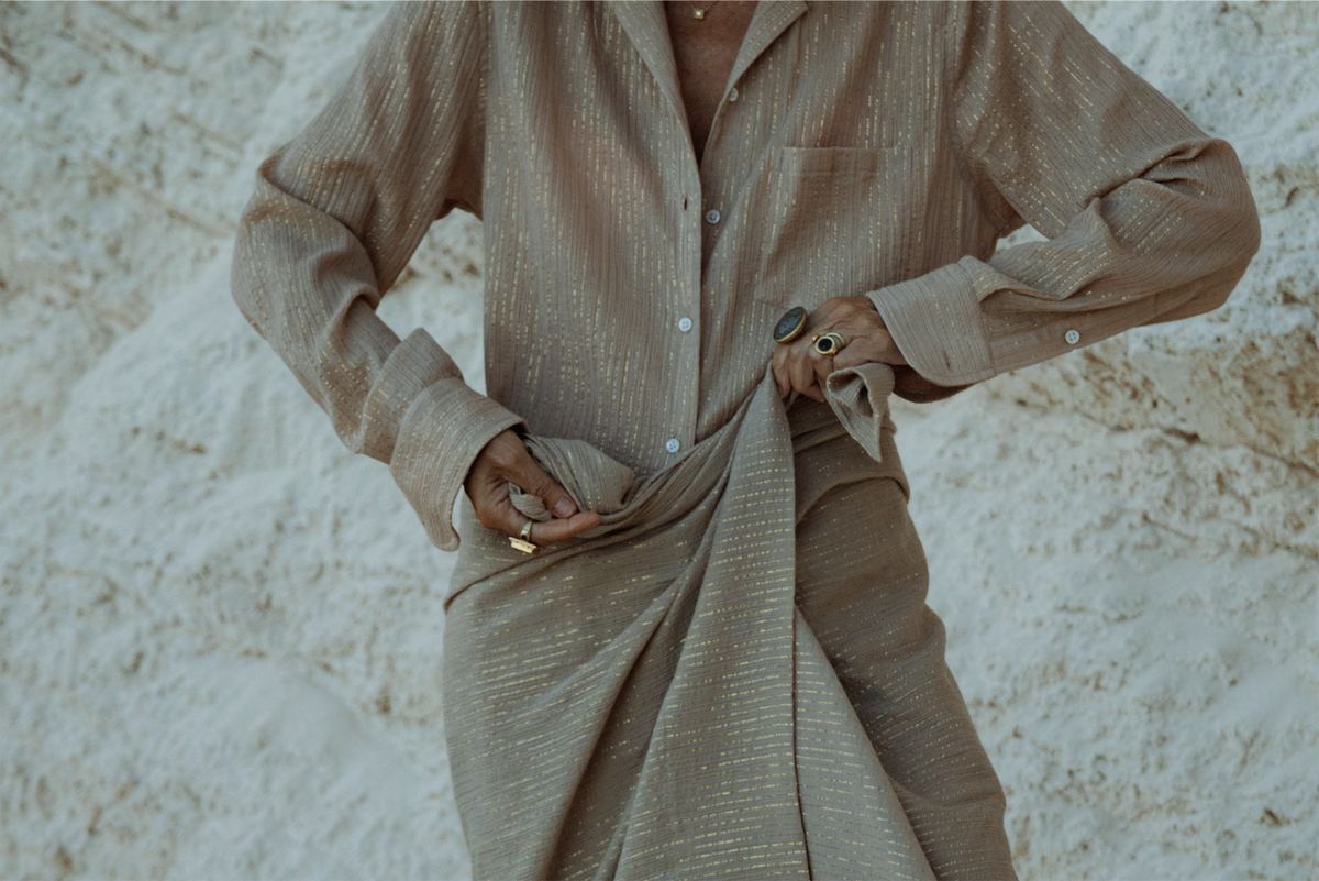 Close crop of hands gathering a textured linen shirt and trousers against white rock