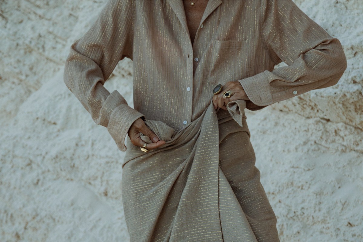 Close crop of hands gathering a textured linen shirt and trousers against white rock
