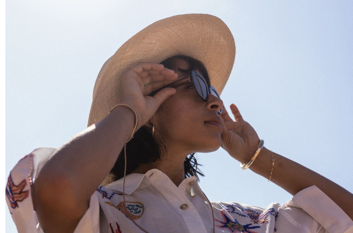 Model shading her eyes beneath a wide straw sun hat in an embroidered blouse