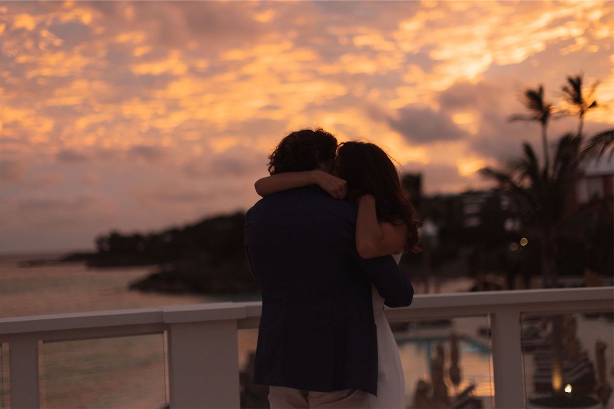 Couple wrapped in an embrace on an oceanfront deck beneath a burning sunset