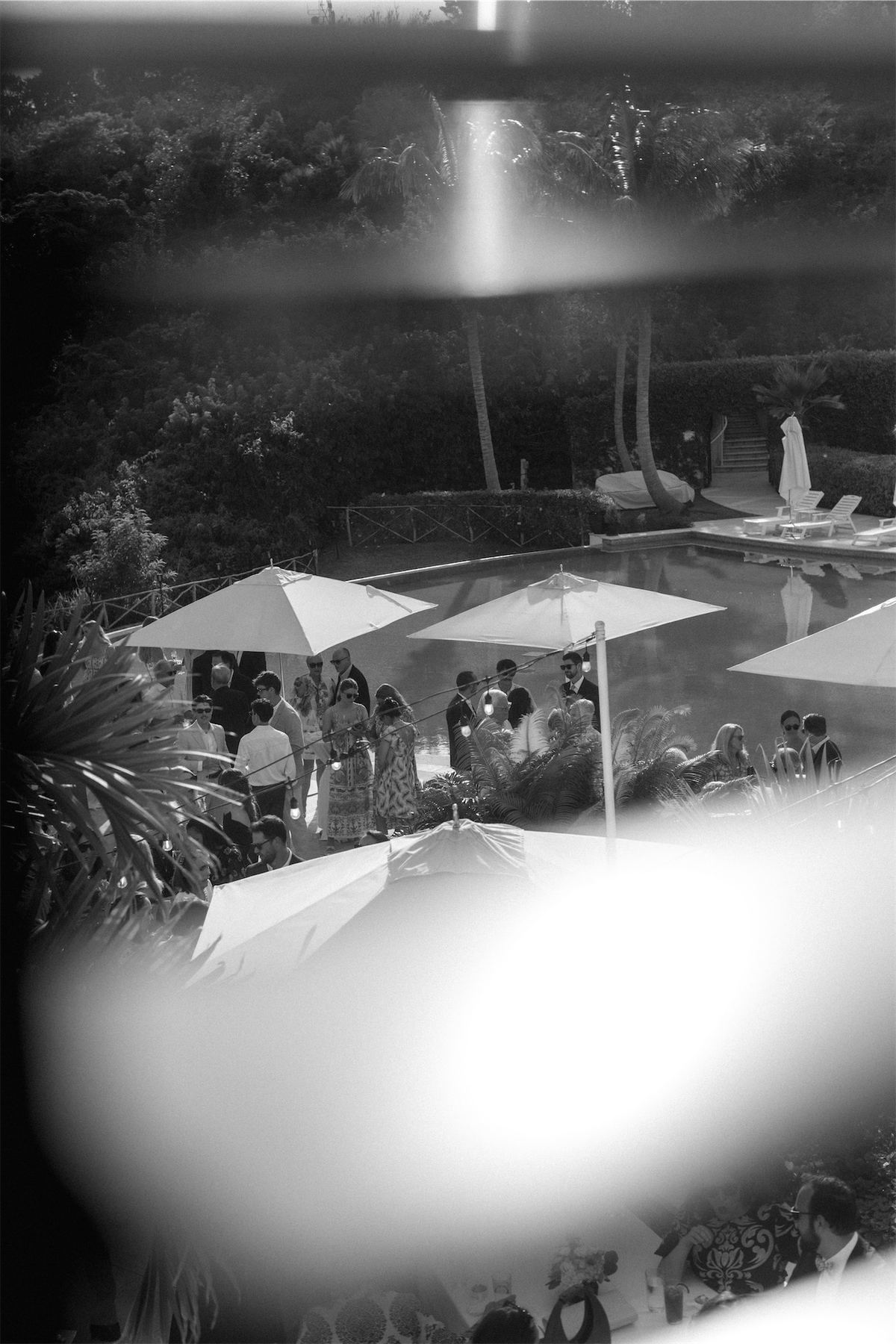 Blurred black and white glimpse of a poolside reception seen past a glass