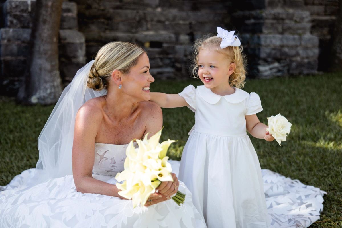 Bride sitting on the grass laughing with the flower girl at the Bermuda church ruins