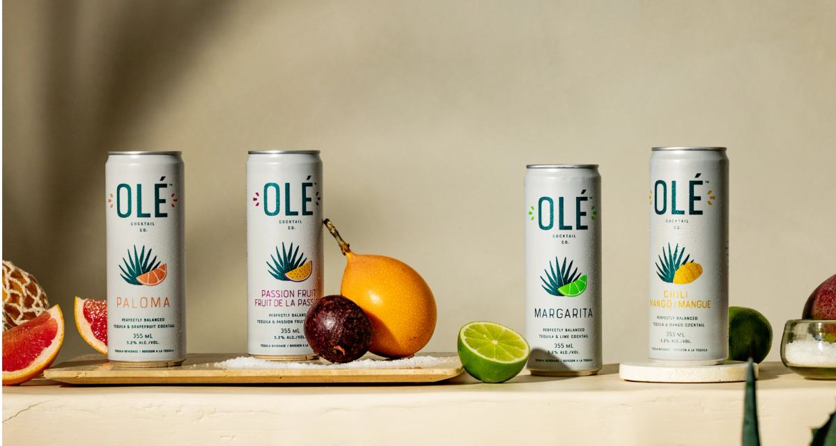 Full lineup of four canned cocktail flavours arranged on a ledge with fresh fruit