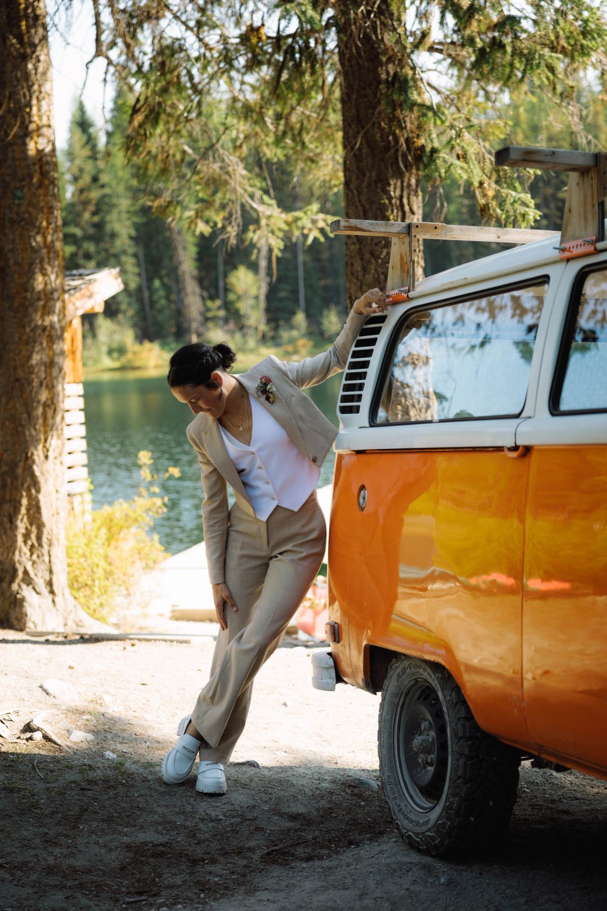 Bride in a linen suit leaning against the open door of the orange camper van