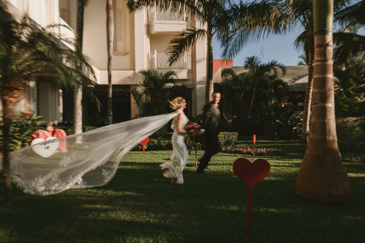 Bride and groom running through palm trees with veil flowing behind at destination wedding