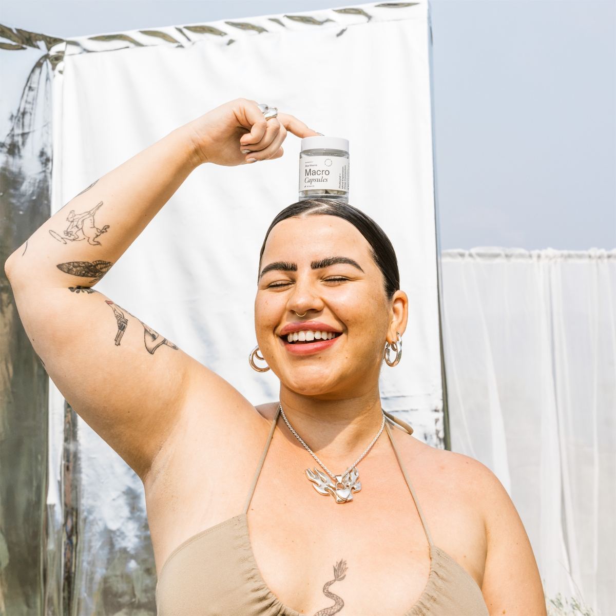 Model raising a Macro Capsules jar overhead, laughing on a draped set