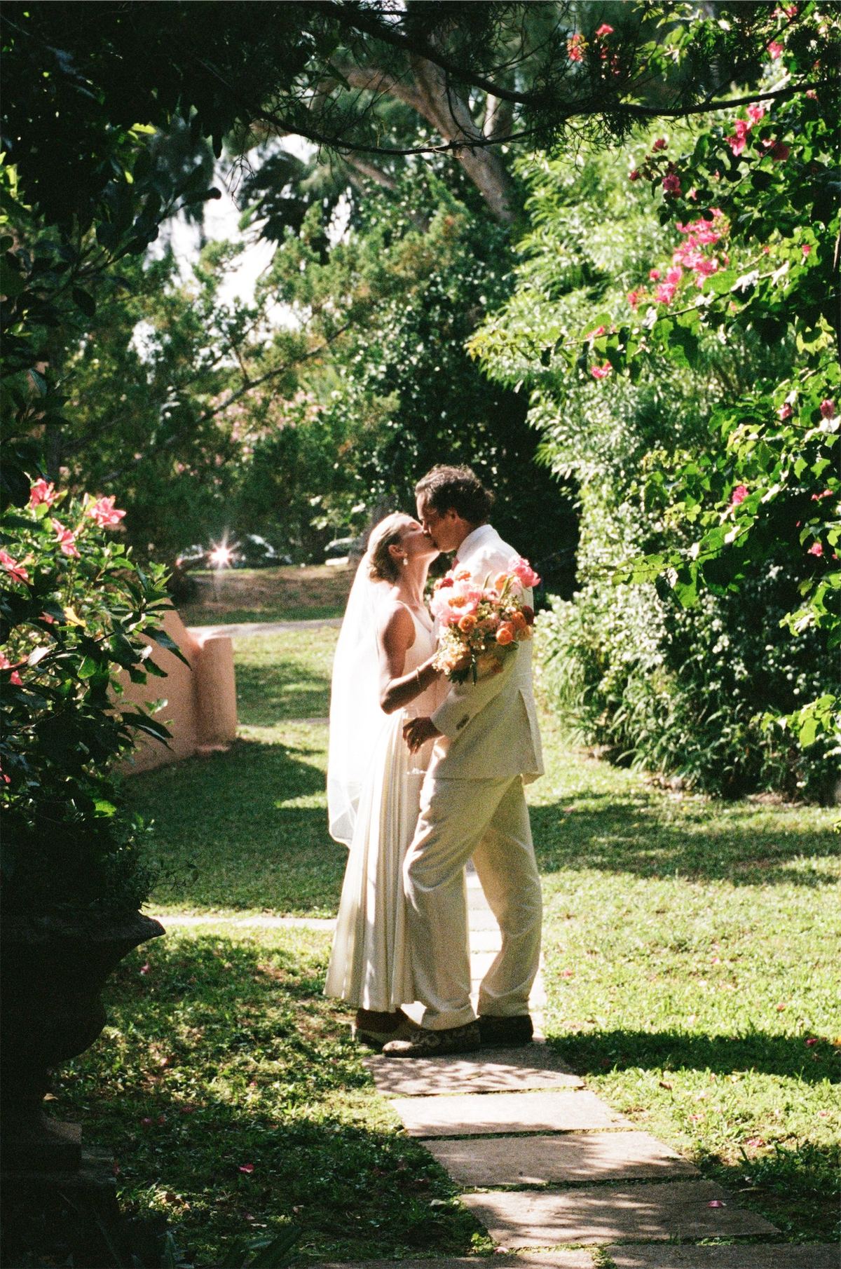 Couple embracing on a garden path framed by hibiscus and palms