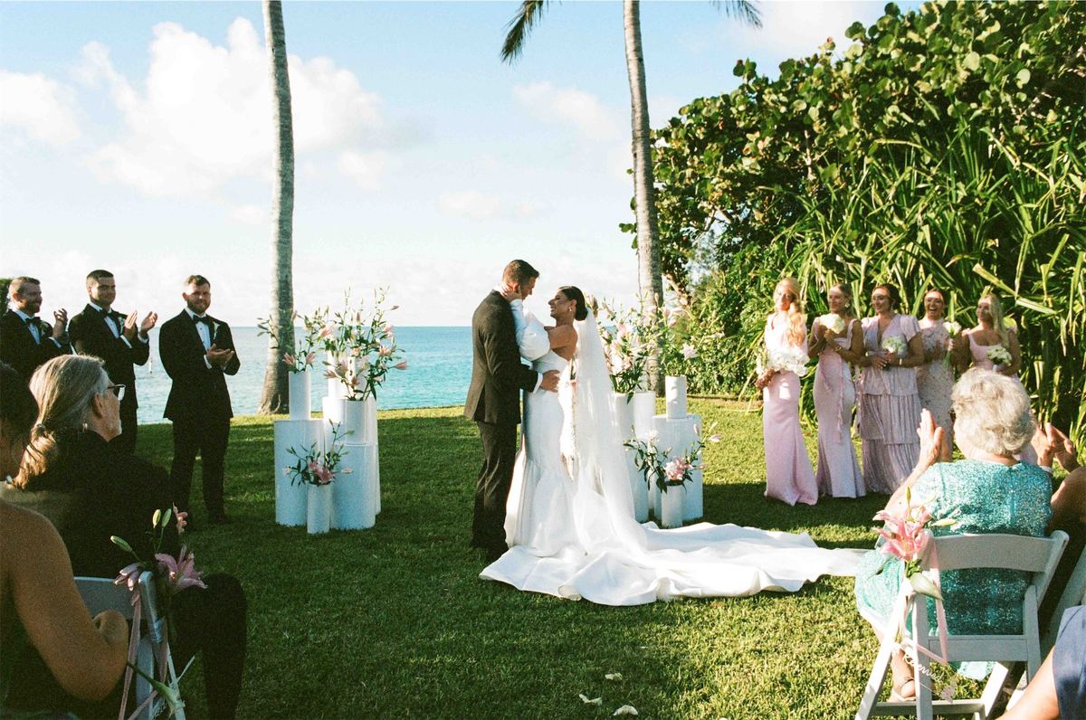 Bride and groom exchanging vows at an outdoor ceremony under palms by the sea